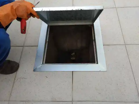 Caixa de gordura embutida no piso de uma cozinha comercial, com a tampa aberta