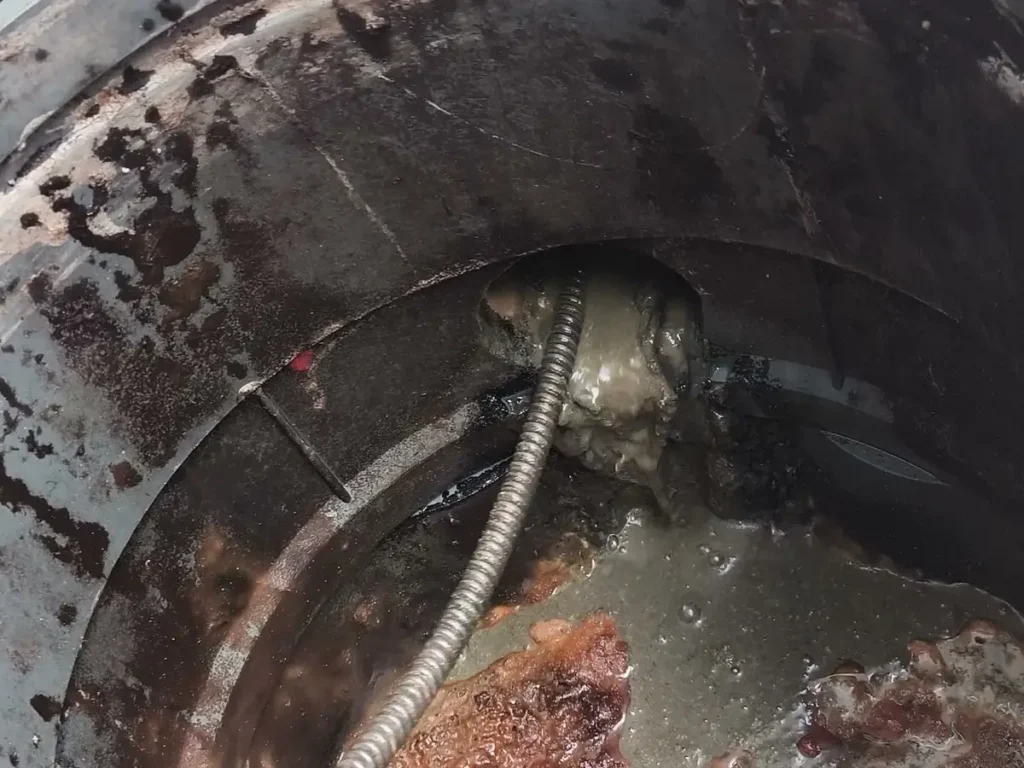 Caixa de gordura redonda aberta, com gordura na superfície e a mola de desentupimento no tubo