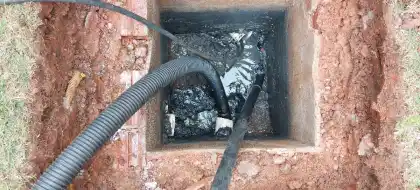 Caixa aberta no terreno com mangueiras de jato e sucção durante uma limpeza de rede em Curitiba