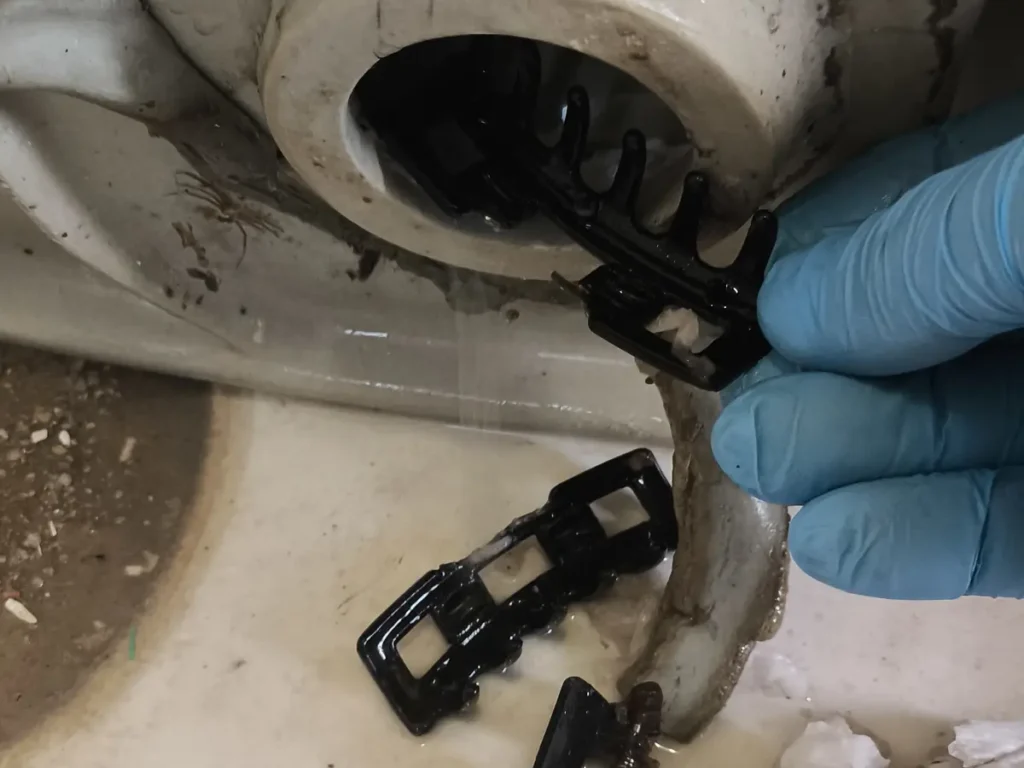 Caixa sifonada aberta no piso do banheiro, com a peça interna sendo retirada para limpeza